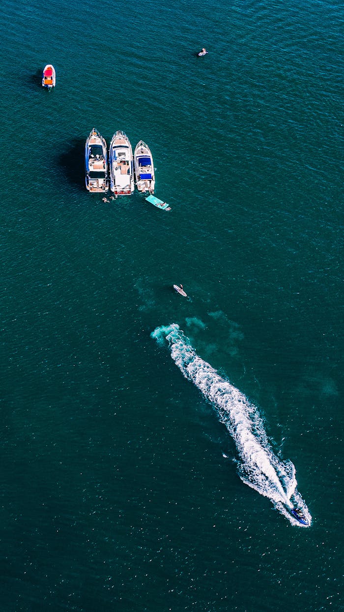 Aerial shot of boats and a jet ski on the open ocean with clear blue water.